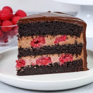 Slice of tall, elegant Chocolate Raspberry Mousse Cake with clear layers and a high-shine mirror glaze.