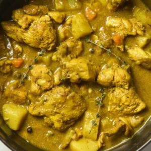 A bowl of authentic Jamaican Curry Chicken served over white rice with fresh thyme garnish.
