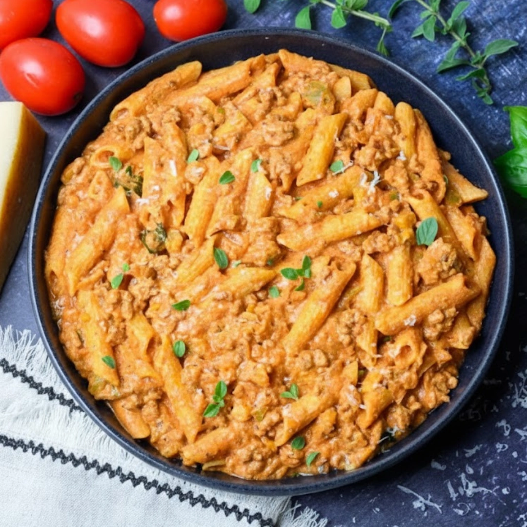 A close-up of a bowl of High Protein Creamy Beef Pasta Recipe topped with fresh basil and parsley.