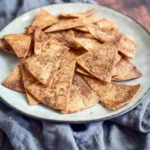 A stack of golden brown Air Fryer Cinnamon Tortilla Chips dusted with cinnamon sugar, ready to be eaten.